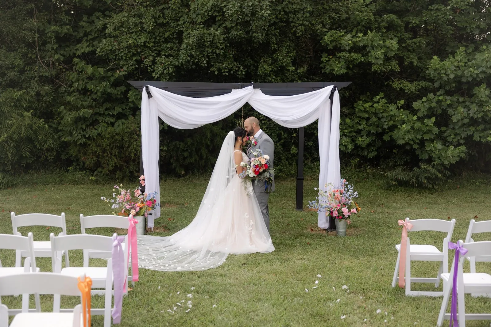 Outdoor ceremony site with white chairs and a floral-draped arch on the lawn at The Heritage Barn