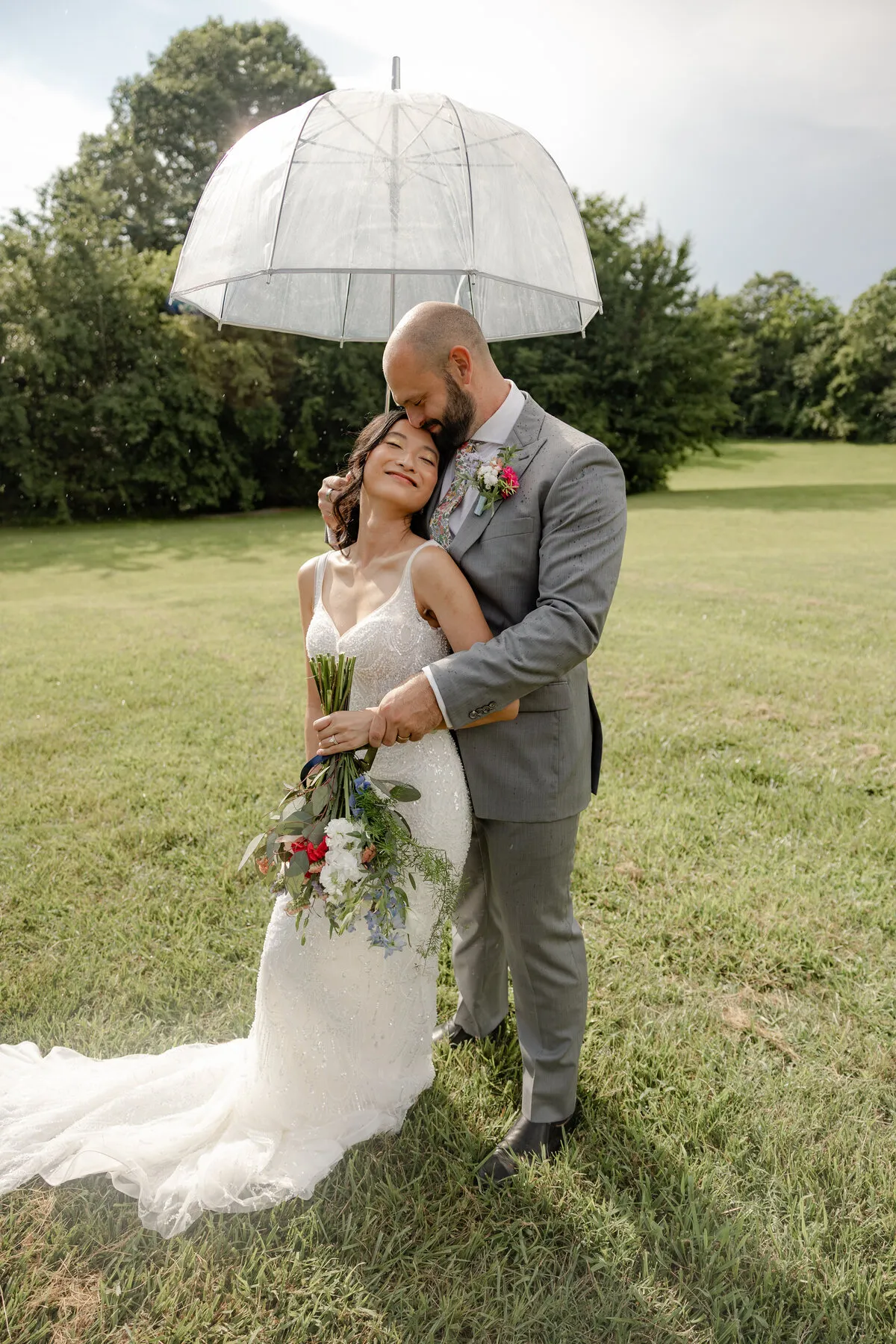 Couple under a clear umbrella on the grounds at The Heritage Barn