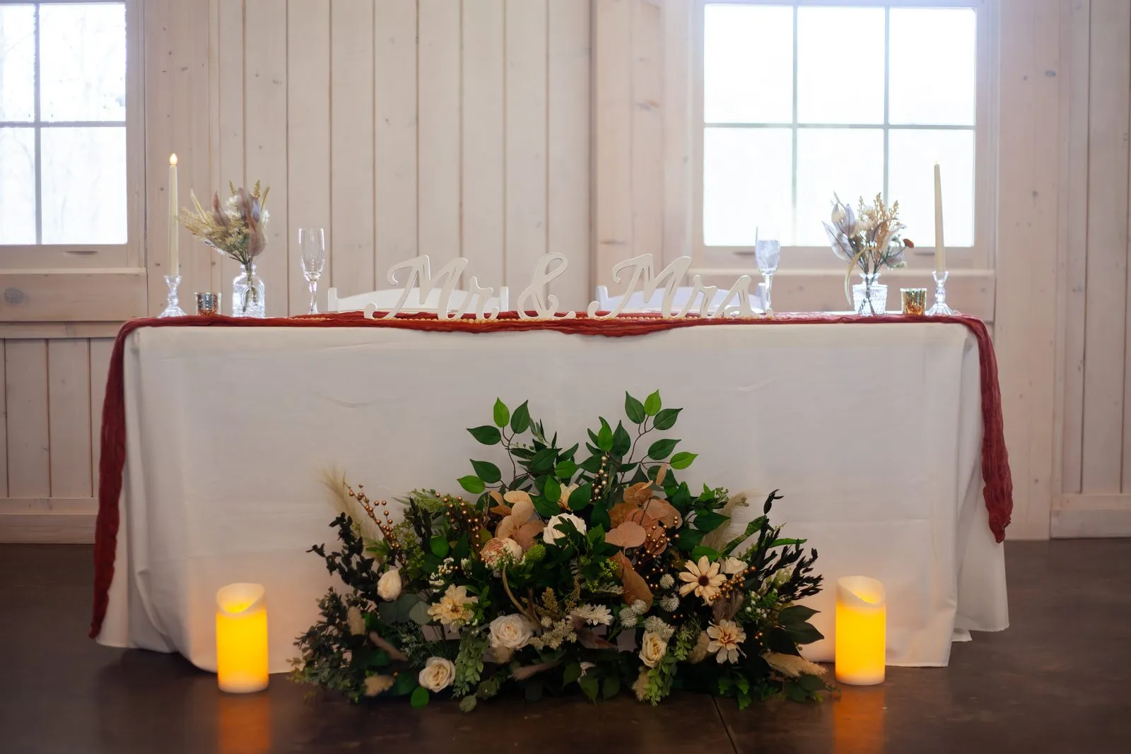 Head table dressed with florals, greenery, and candlelight in the barn at The Heritage Barn