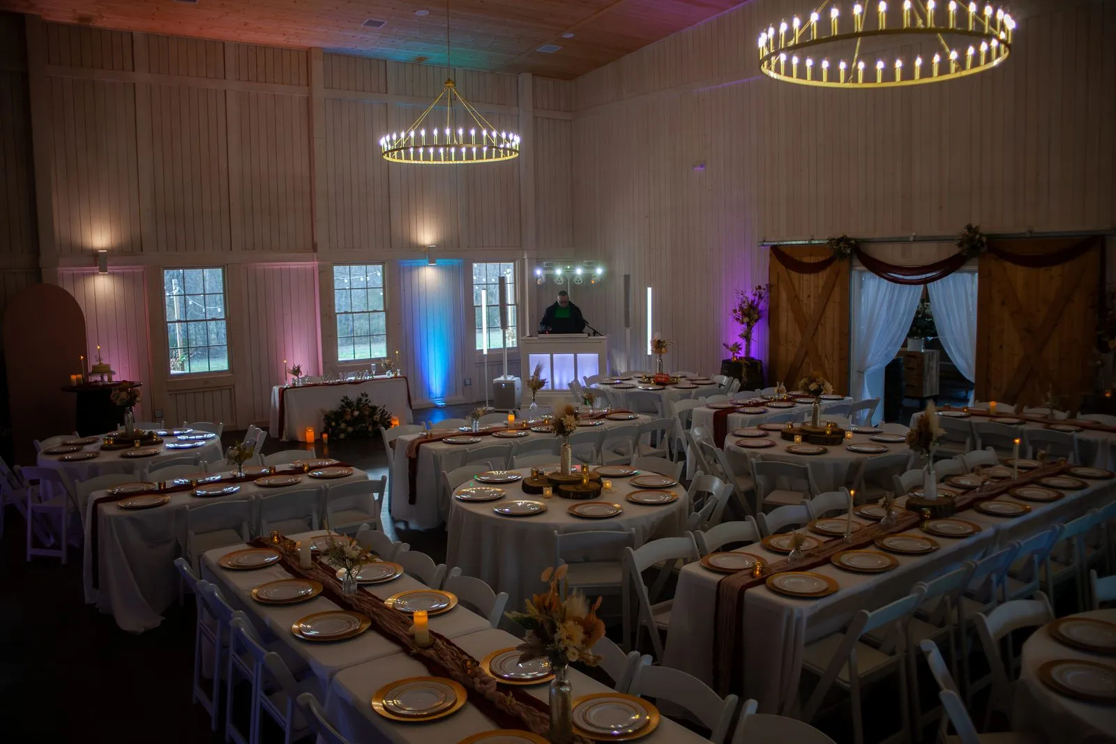 Reception tables glowing beneath chandeliers inside the barn at The Heritage Barn
