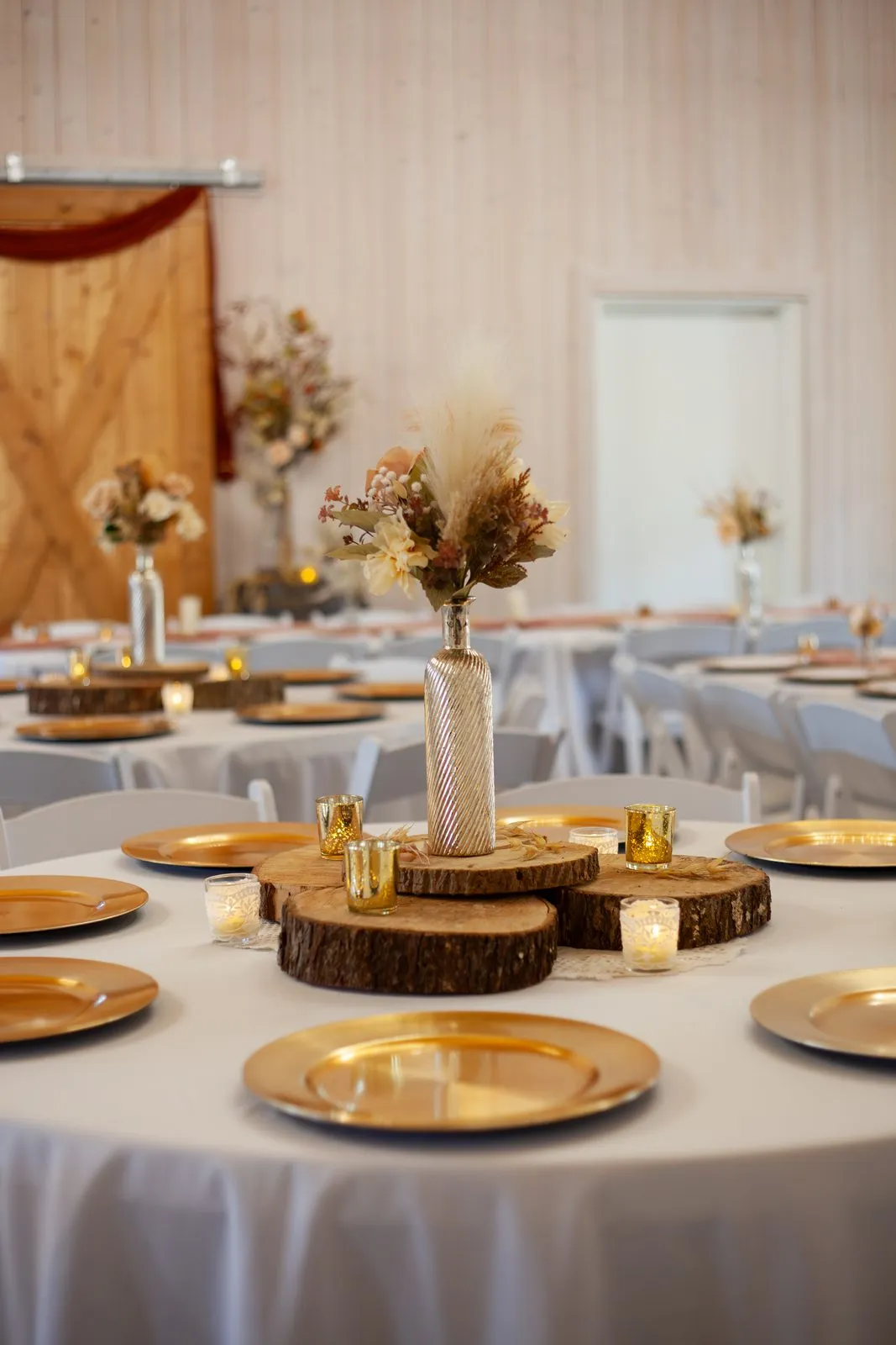 Candlelit round table with gold chargers and wood-slice details at The Heritage Barn